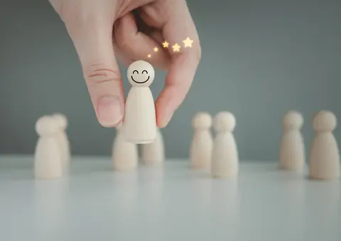 Una mano coloca una ficha con una carita sonriente sobre una fila de figuras de madera